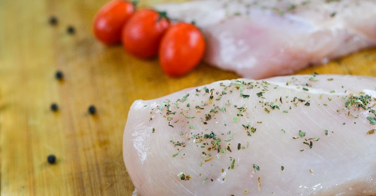 Fresh uncooked chicken breasts sprinkled with herbs, accompanied by cherry tomatoes on a wooden board.