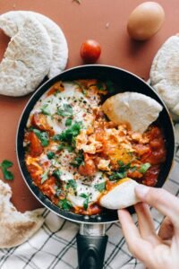 Savor a classic Shakshuka dish with vibrant tomatoes, eggs, and herbs served with fresh pita bread.